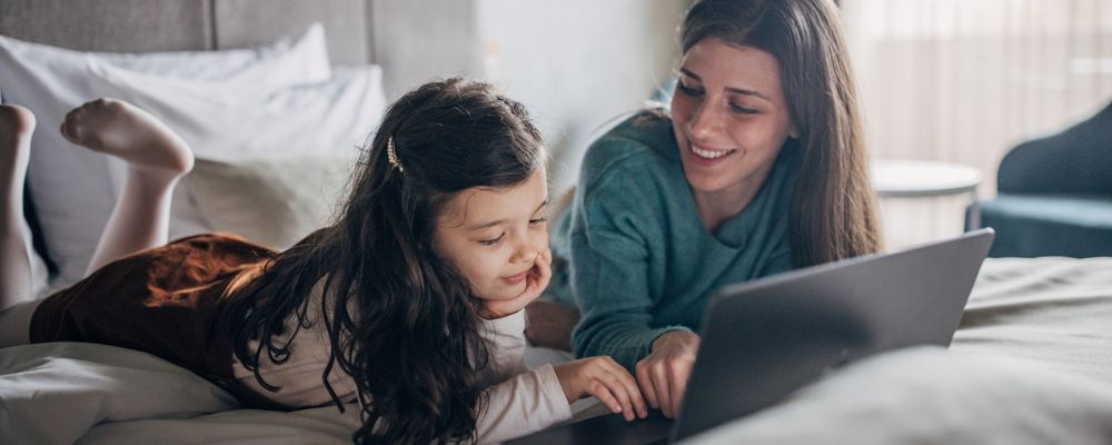 Mother and daughter looking at laptop while lying on bed